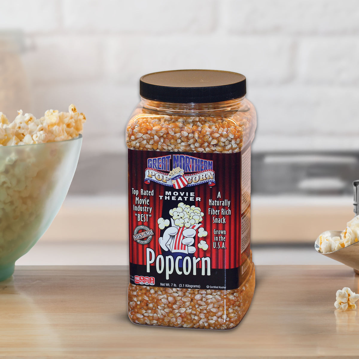 Jar of popcorn kernels with a bowl of popcorn on a kitchen counter