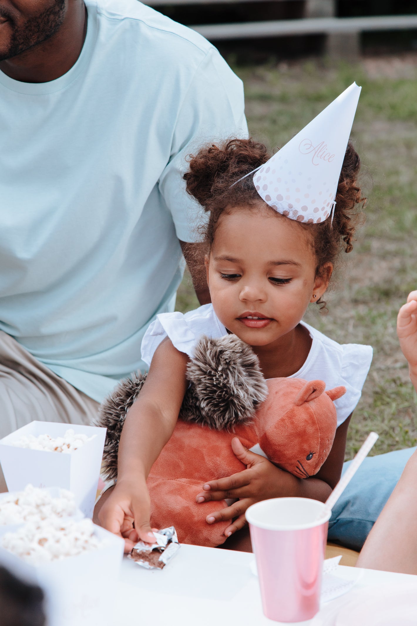 Birthday party hosts popcorn and a young girl holds her stuffed squirrel animal while enjoying a snack.